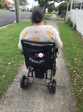 photo of a lady sitting in a motor scooter from behind and on a residential footpath