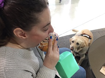 a photo of Em eating a Cinnabon with dog guide Annie watching