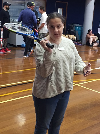 A photo of a young  girl who is blind standing with a tennis racket in hand and facing camera