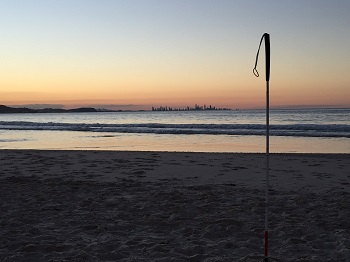 a photo of a Beachside sunset image over the ocean with long cane seen right of image