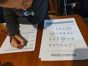 a photo of Mason attending to Braille Dot Leaning sheets with a pencil