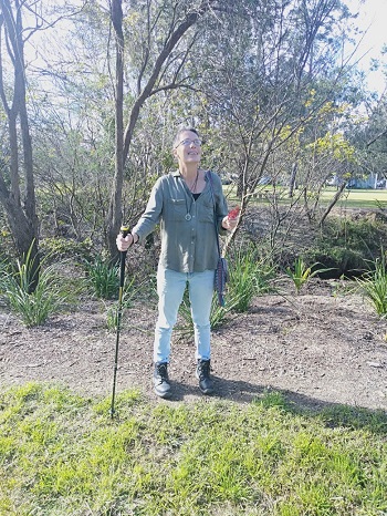 a photo of Lisa standing in a bush setting holding her hiking pole and looking upwards