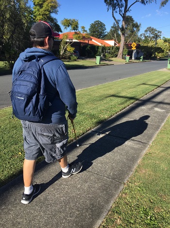 a picture Side and rear profile of a man walking along a residential footpath using his long cane