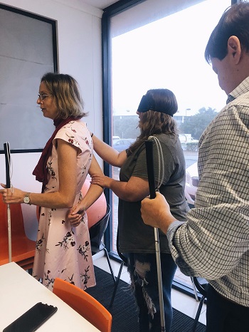 image shows Kim guiding one of the radio hosts at radio studio, with two other staff behind applying sighted guide