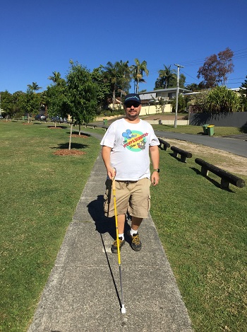 a picture of Justin walking on a path with a yellow long cane